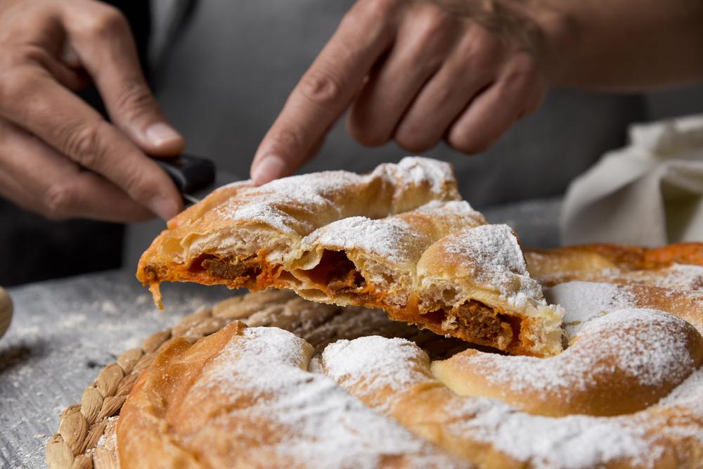 Close up de jóven que sirve una pieza de una ensaimada, una pastelería típica de Mallorca, España, llena de sobrasada, colocada sobre una mesa rústica de madera.